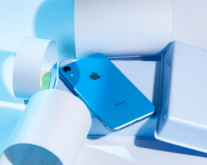 a blue iphone sitting in a box next to a roll of toilet paper