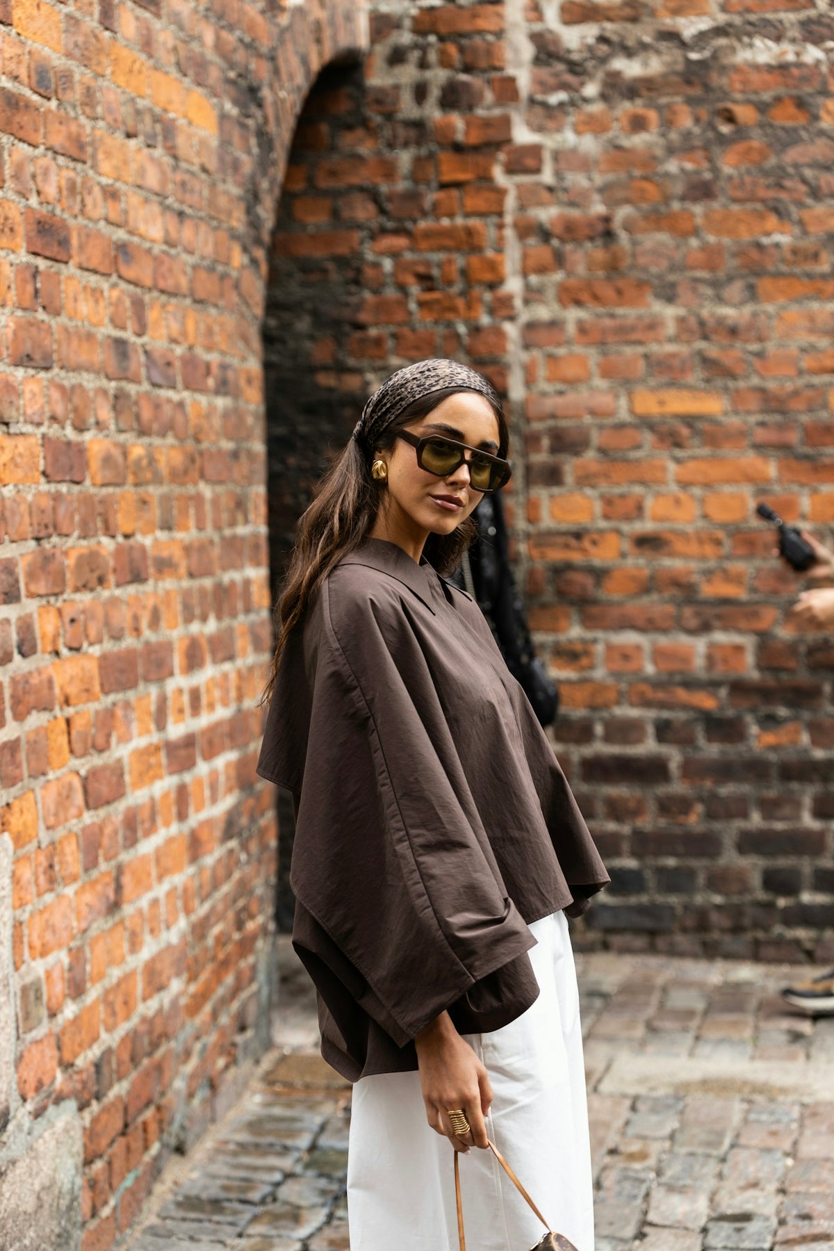 Woman in stylish outfit posing against brick wall