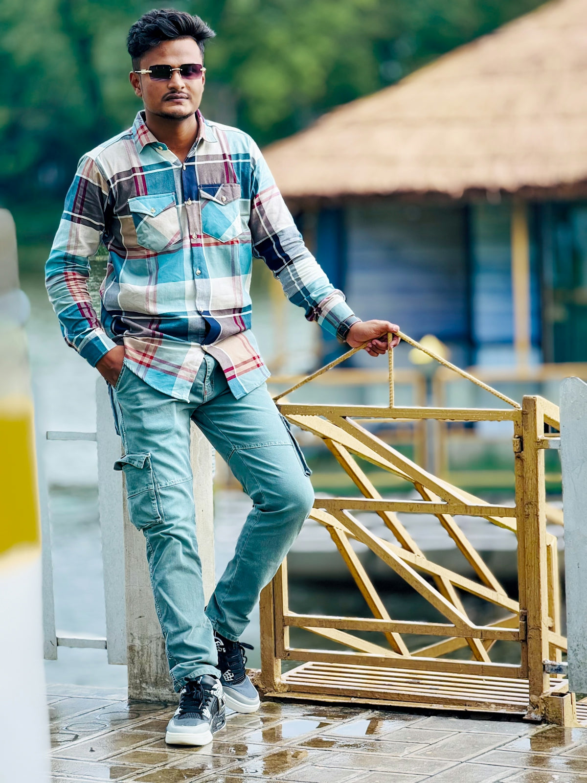 Stylish young man in plaid shirt and sunglasses by water.